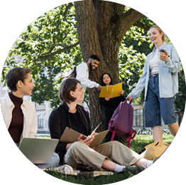 Four people are sitting on the grass, using their laptops. One woman is standing and holding a cell phone. They are surrounded by backpacks and handbags. AI generated content
